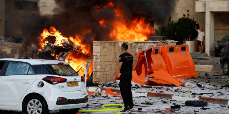 A man stands on a road as fire burns after rockets were launched from the Gaza Strip, in Ashkelon, Israel October 7, 2023. REUTERS/Amir Cohen