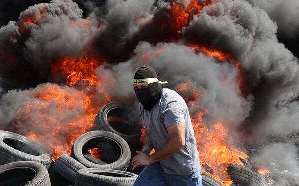 TOPSHOT - A protester runs near burning tyres during clashes with Israeli forces following a demonstration against the expropriation of Palestinian land by Israel in the village of Kfar Qaddum, in the occupied West Bank on September 29, 2023. (Photo by Jaafar ASHTIYEH / AFP)